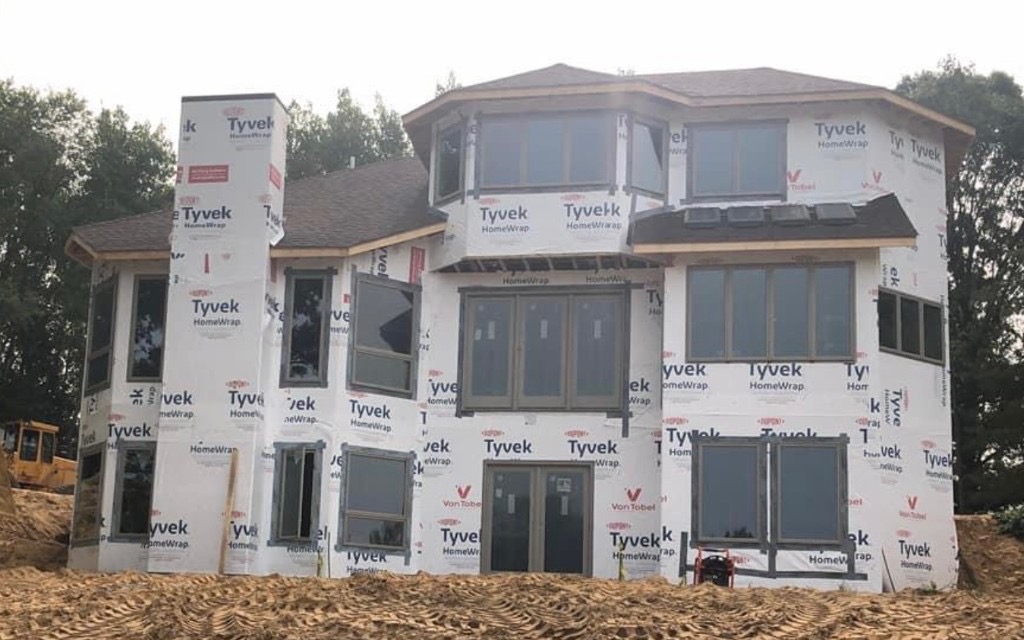 Two-story custom home dried-in with Tyvek wrap, brown roof shingles, and dark-framed windows