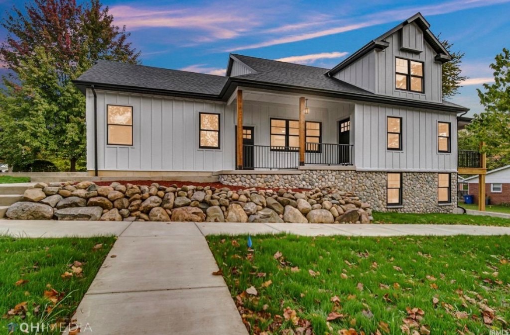 Modern farmhouse custom home with white board-and-batten siding and stone foundation at twilight