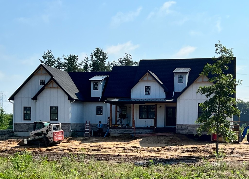 Modern farmhouse custom home with white siding, stone veneer, and standing seam metal porch roof