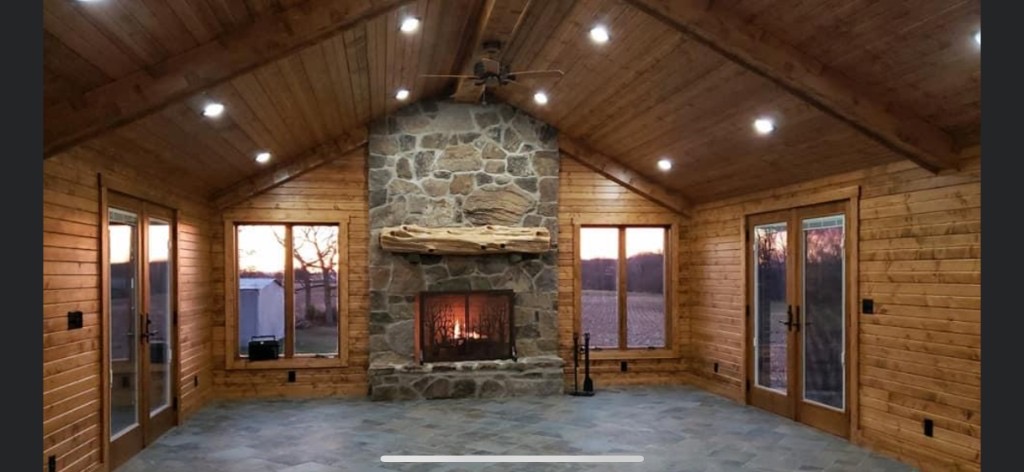 Rustic cabin interior with vaulted wood ceiling, stone fireplace, and slate tile floor